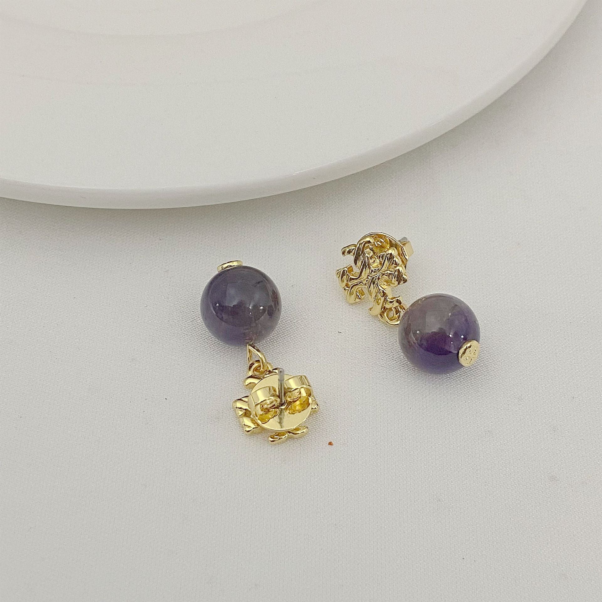 Pair of gold earrings with purple beads on a white surface