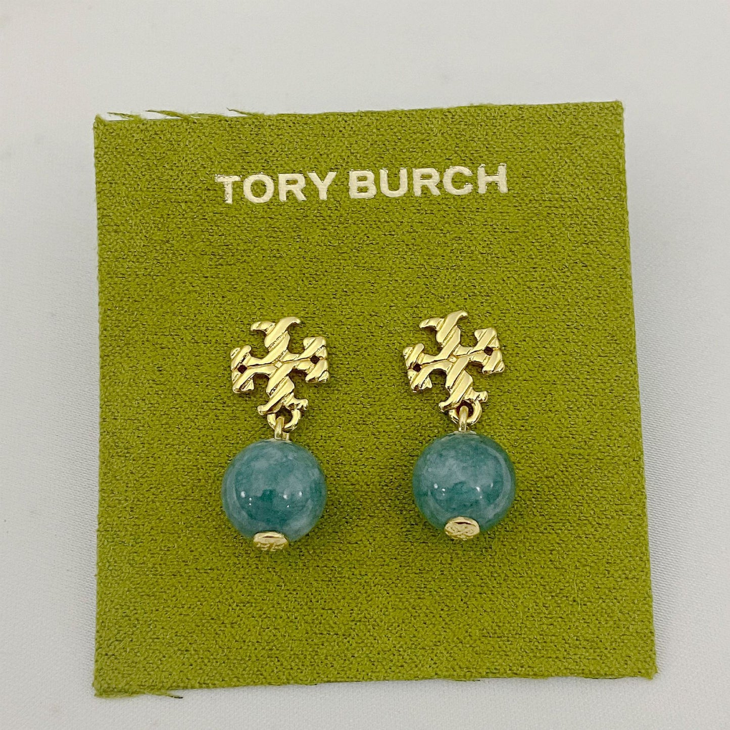 Gold earrings with turquoise beads on a Tory Burch branded green card.