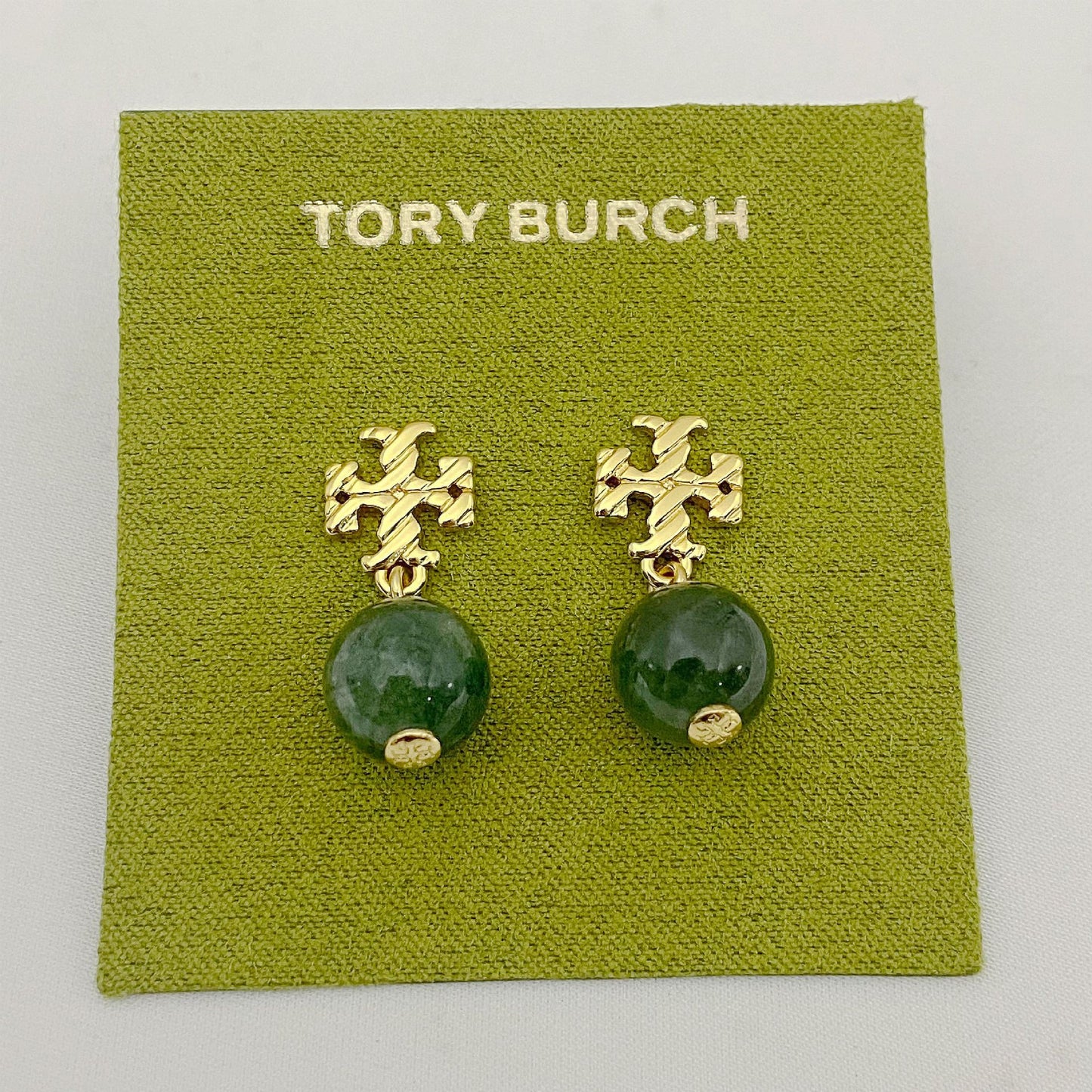 Gold earrings with green beads on a Tory Burch branded card.