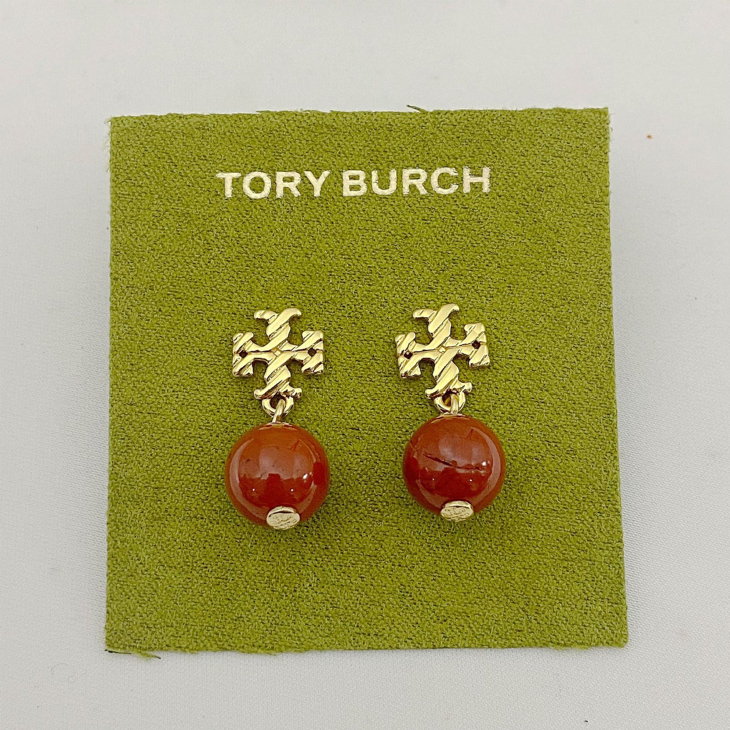 Tory Burch earrings with gold designs and red beads on a green card.