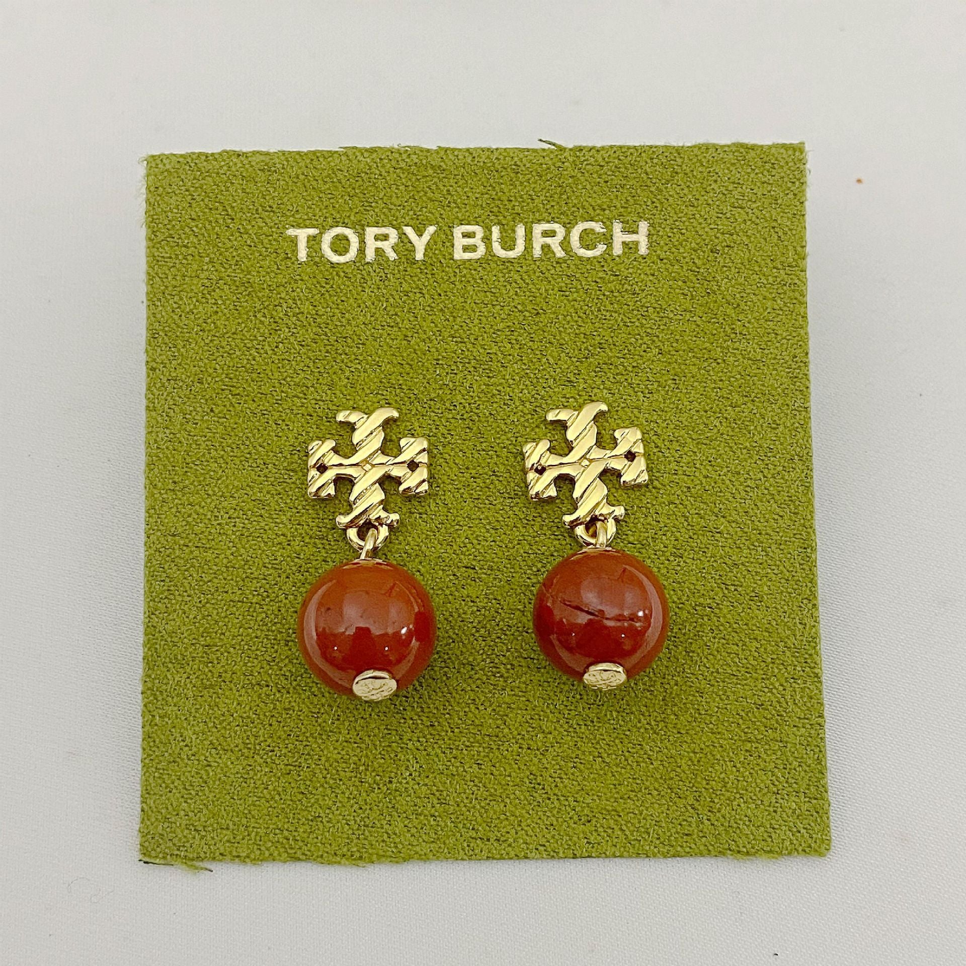 Tory Burch earrings with gold designs and red beads on a green card.