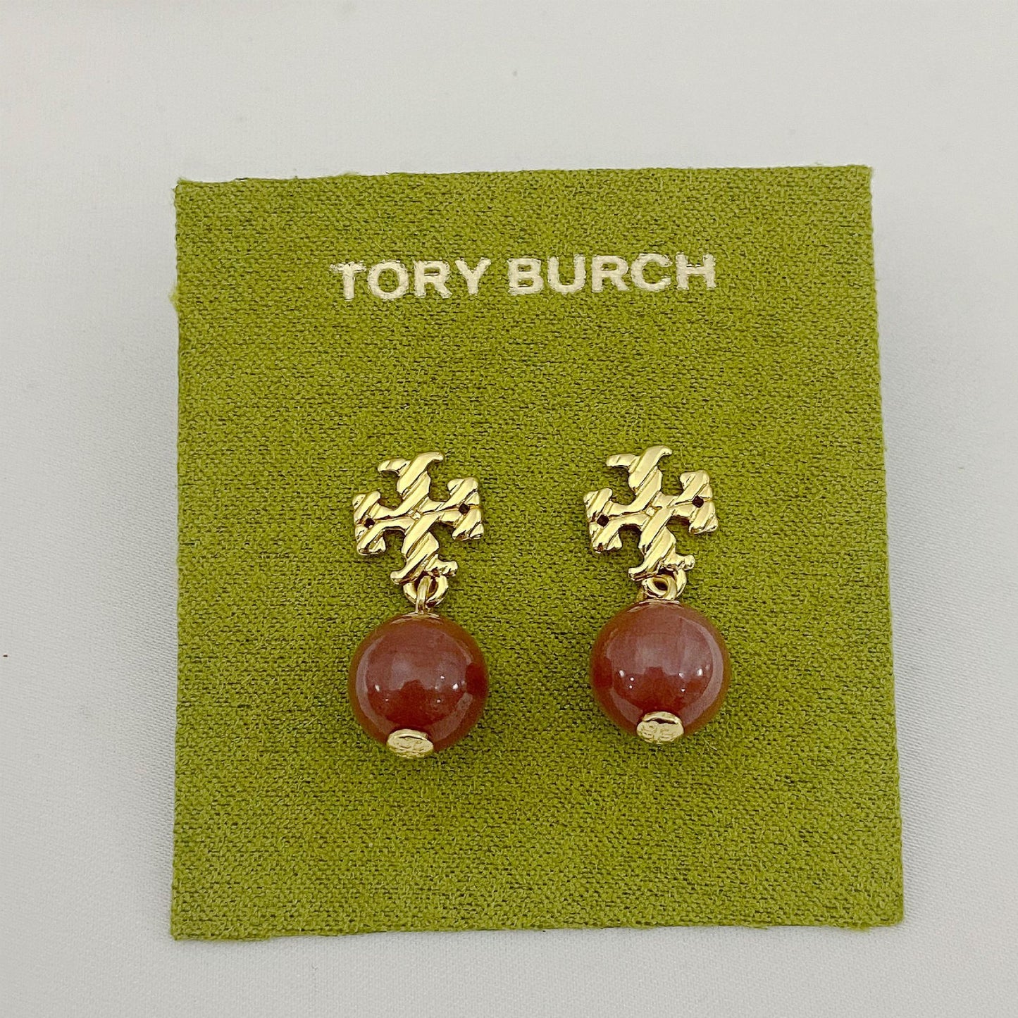 Tory Burch earrings with gold tops and red beads on a green card.