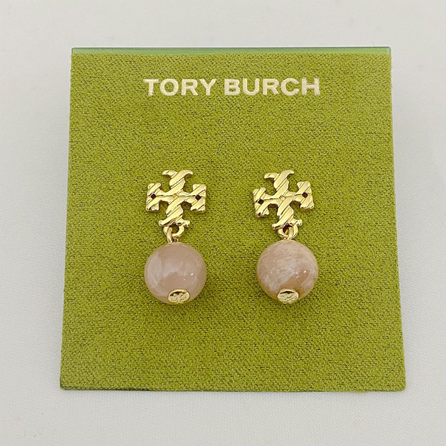 Gold earrings with pink beads on a Tory Burch branded card.