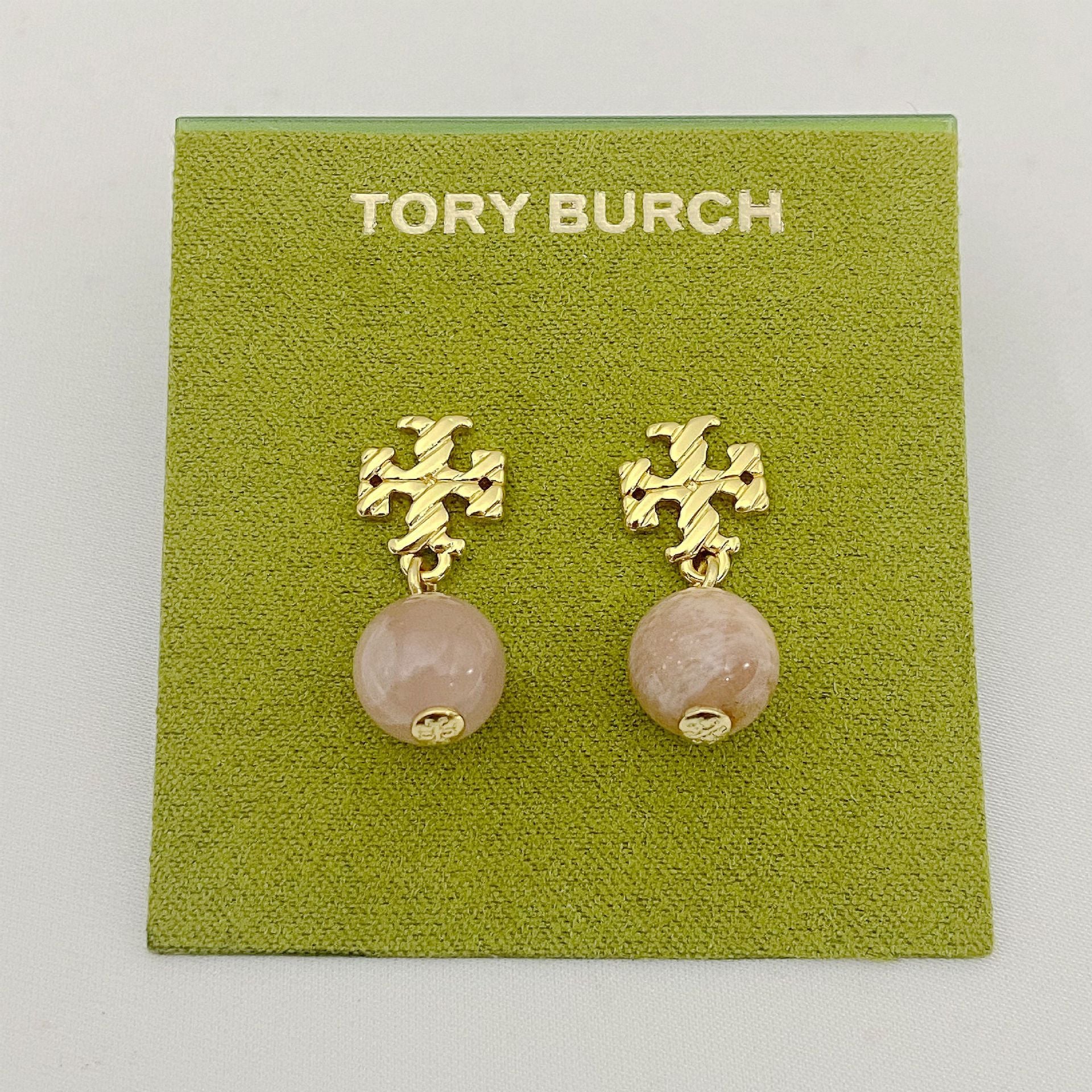 Gold earrings with pink beads on a Tory Burch branded card.