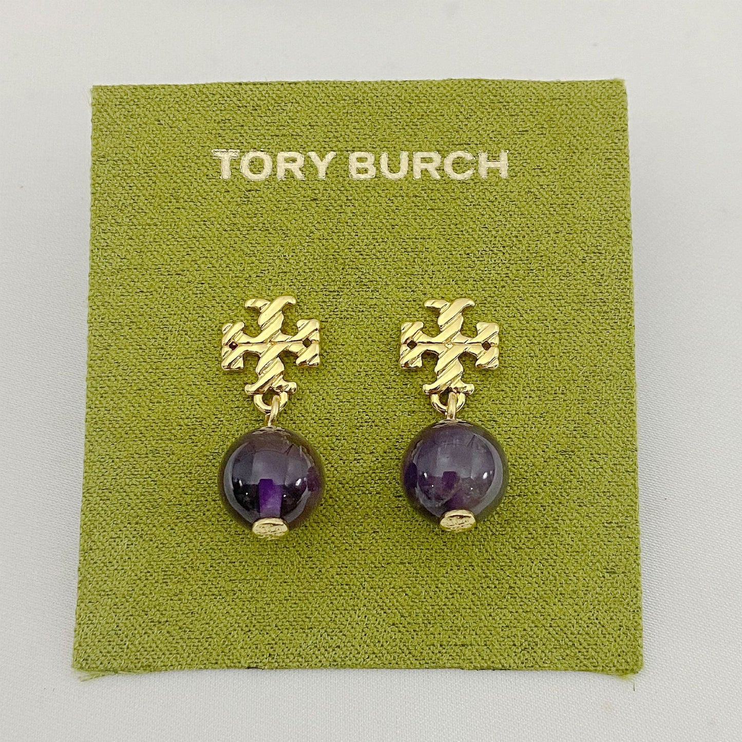 Gold earrings with purple beads on a Tory Burch branded card.