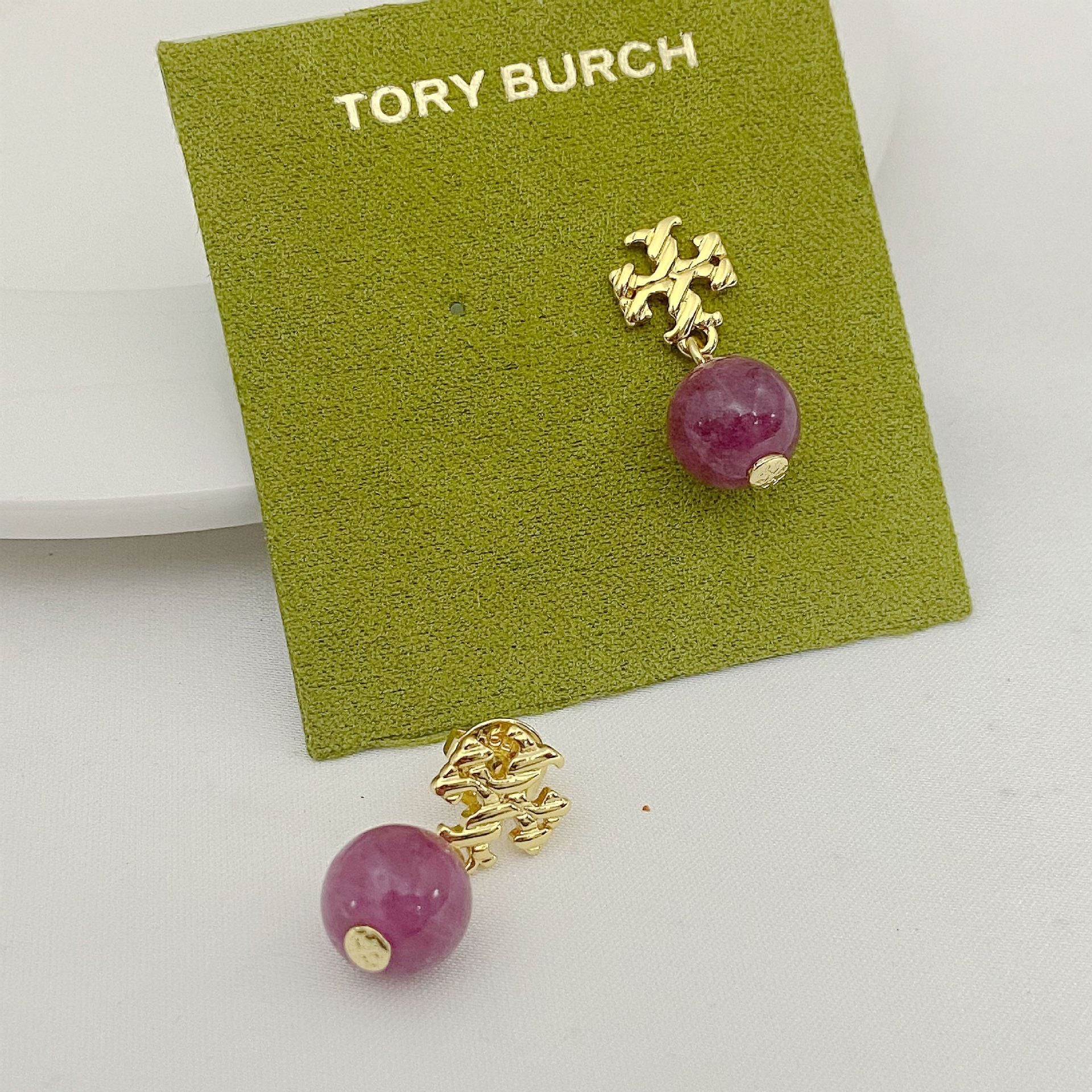 Gold earrings with pink beads on a Tory Burch branded card.
