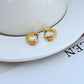 Tory Burch-inspired Kira Enamel Huggie Earrings in [Color Name] displayed on a soft-toned background, highlighting the curved gold hoop and vibrant enamel band."