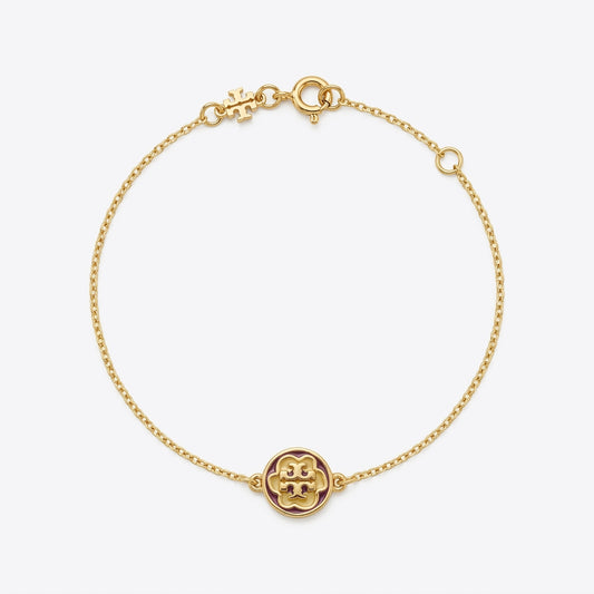 A delicate gold chain bracelet featuring a small circular medallion with a raised monogram logo at the bottom, displayed on a clean light gray background.