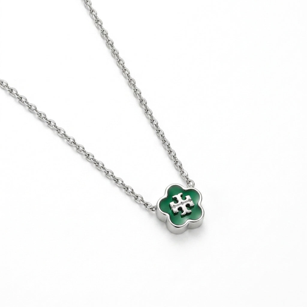A silver-tone chain necklace with a four-petal flower pendant featuring a vibrant green enamel center and a silver-tone monogram logo.