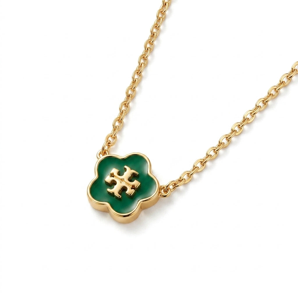 A gold chain necklace featuring a four-petal clover pendant with a glossy green enamel center and a gold interlocking T logo, shown on a clean white background.