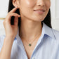 A close-up lifestyle shot of a woman wearing a delicate gold necklace with a green and gold floral pendant, paired with a blue and white striped button-down shirt.