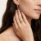 A close-up lifestyle shot of a woman wearing a gold ring with a starburst design on her ring finger, alongside a matching gold bar earring.