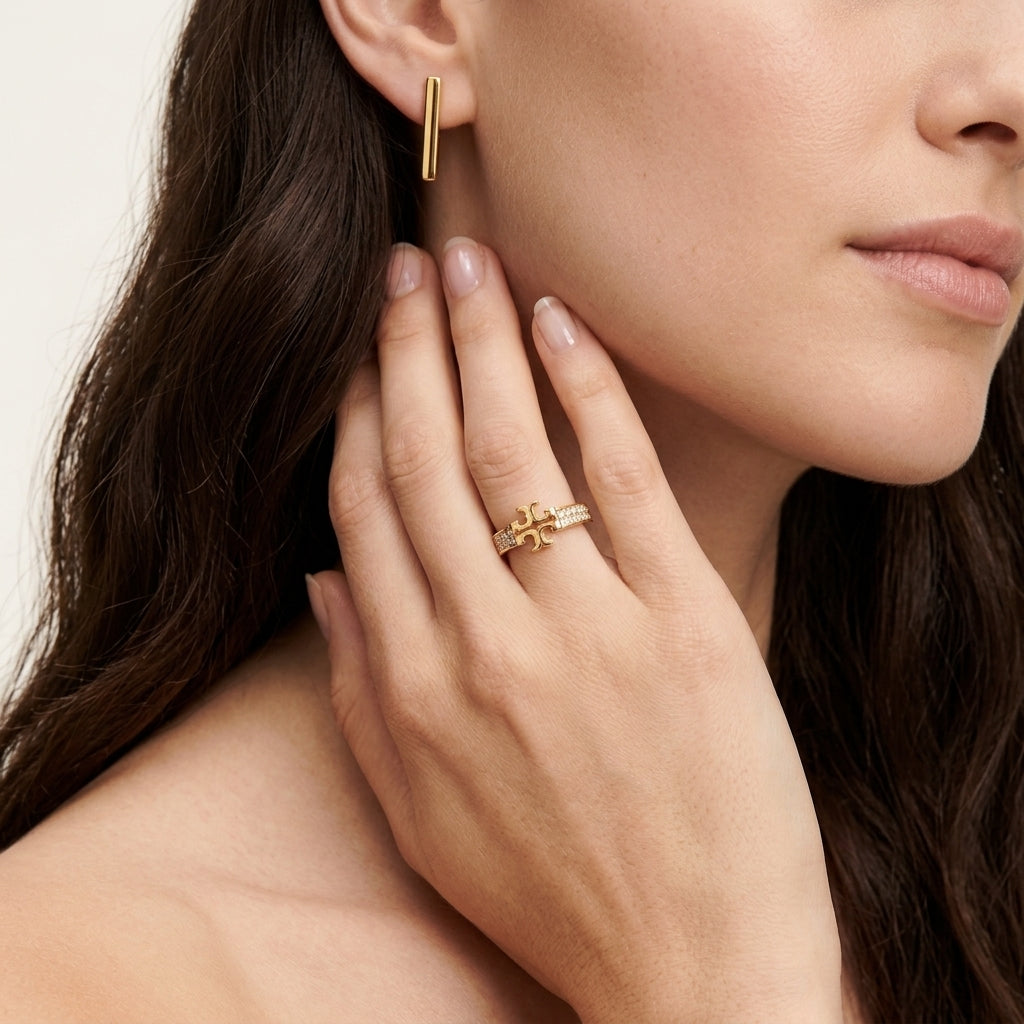 A close-up lifestyle shot of a woman wearing a gold ring with a starburst design on her ring finger, alongside a matching gold bar earring.