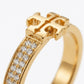 A gold ring featuring a geometric cross-like top and a curved band set with clear pavé stones, shown on a clean white background.