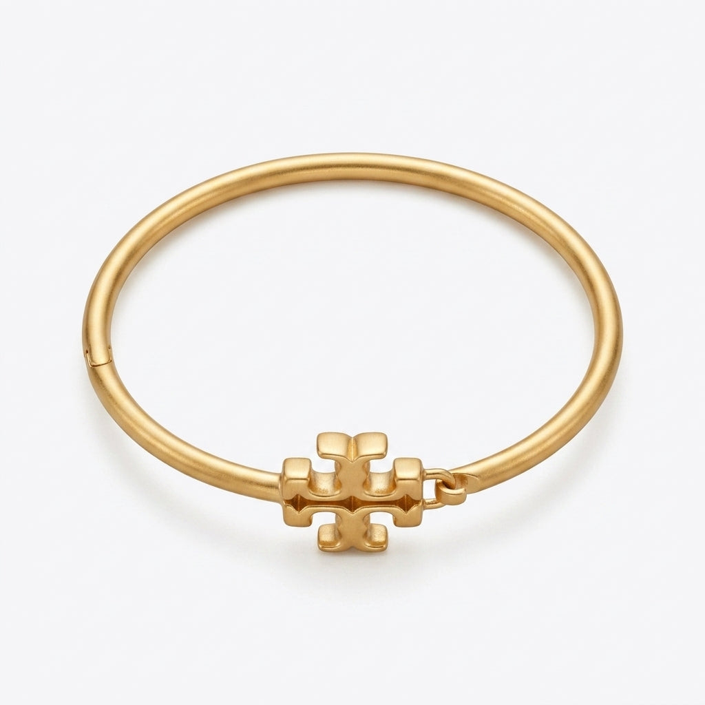 A gold bangle bracelet with a small geometric logo charm, displayed on a clean white background.