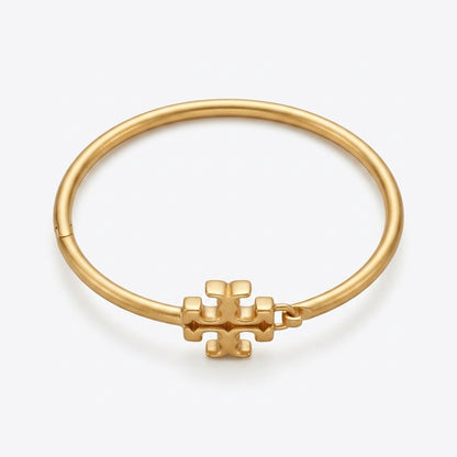 A gold bangle bracelet with a small geometric logo charm, displayed on a clean white background.