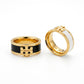 Two gold rings with black and white enamel inlays, each featuring a gold monogram logo on the front, displayed on a clean white background.