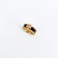 A gold ring with a black enamel inlay and a central interlocking monogram design, photographed on a clean white background.