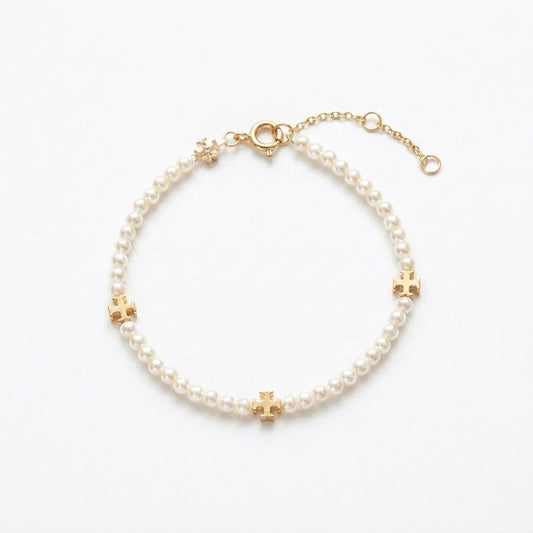 A delicate pearl bracelet with gold-tone cross and flower accents, displayed on a clean white background.