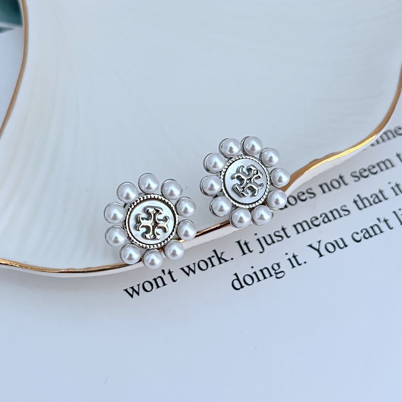 Both studs displayed face-up on a soft, light background (ivory or pale green), highlighting the floral shape and central pearl.