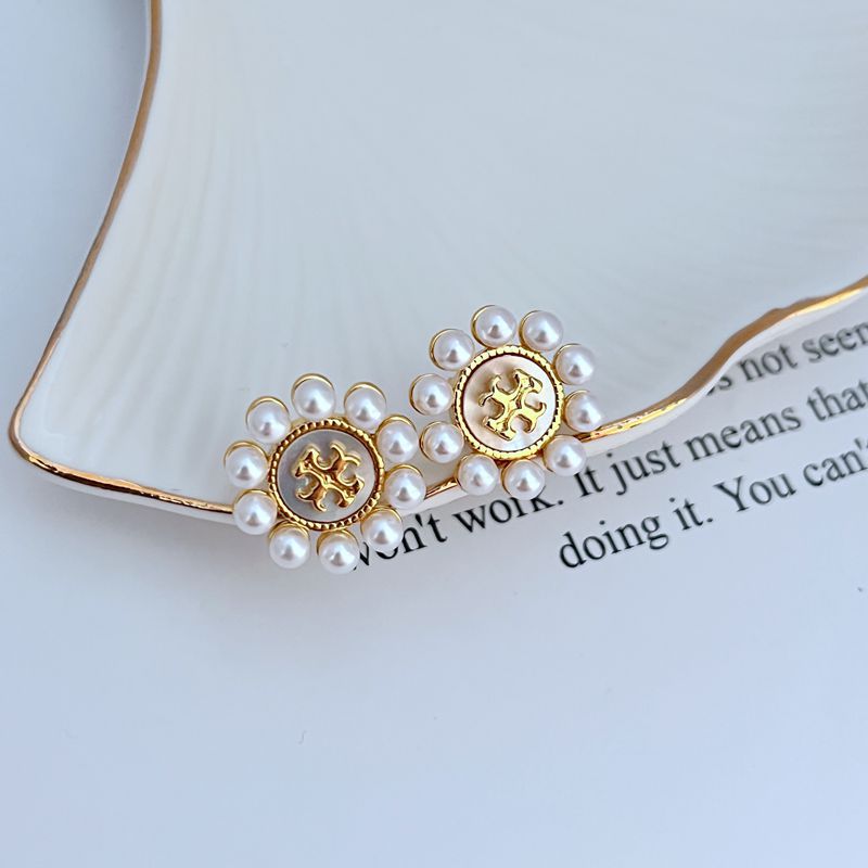 Both studs displayed face-up on a soft, light background (ivory or pale green), highlighting the floral shape and central pearl.
