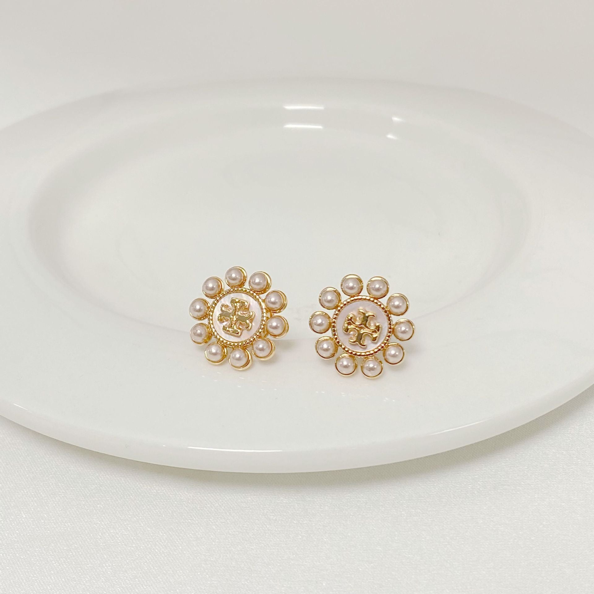 Both studs displayed face-up on a soft, light background (ivory or pale green), highlighting the floral shape and central pearl.