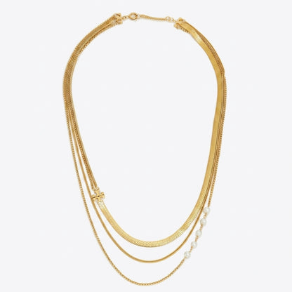 A gold multi-strand necklace featuring three layered chains, including a textured snake chain, a delicate cable chain, and a fine chain accented with small white pearls, shown on a plain white background.