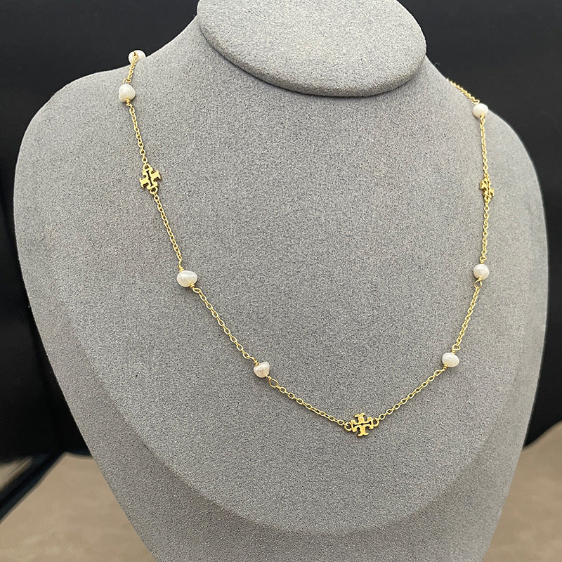 The necklace laid flat on a soft, textured slate-gray background, clearly displaying the two charms (pearl and logo) spaced evenly along the delicate chain.