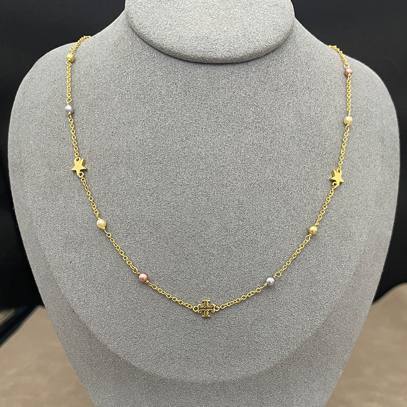 The necklace laid flat on a soft, textured slate-gray background, clearly displaying the two charms (pearl and logo) spaced evenly along the delicate chain.