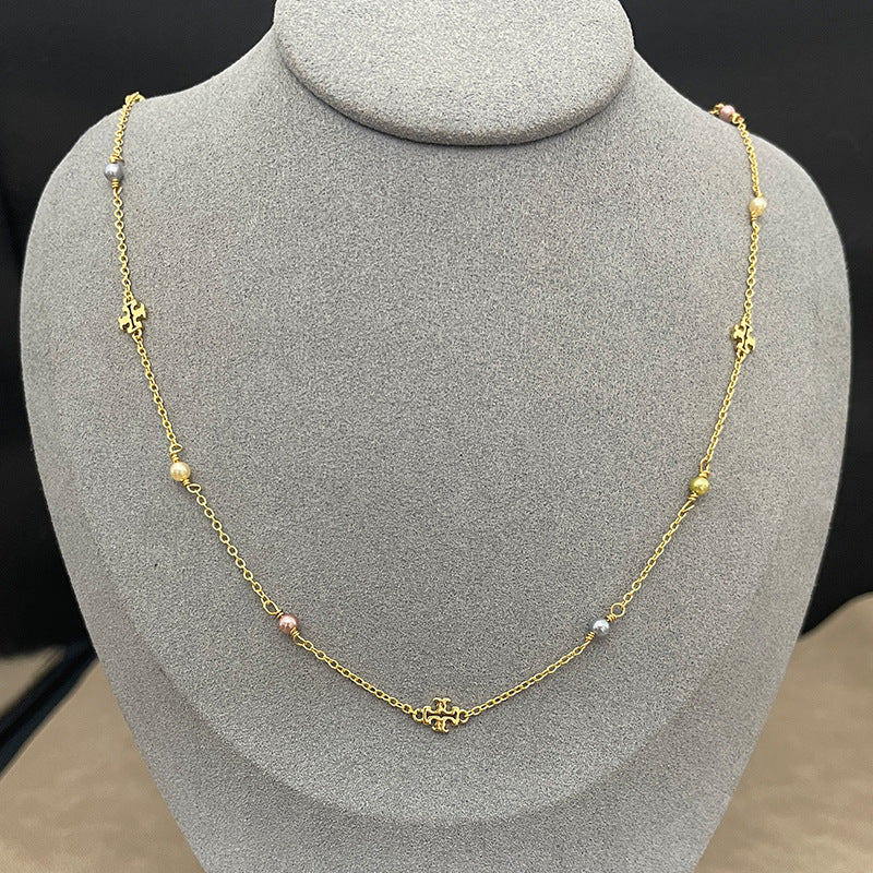 The necklace laid flat on a soft, textured slate-gray background, clearly displaying the two charms (pearl and logo) spaced evenly along the delicate chain.