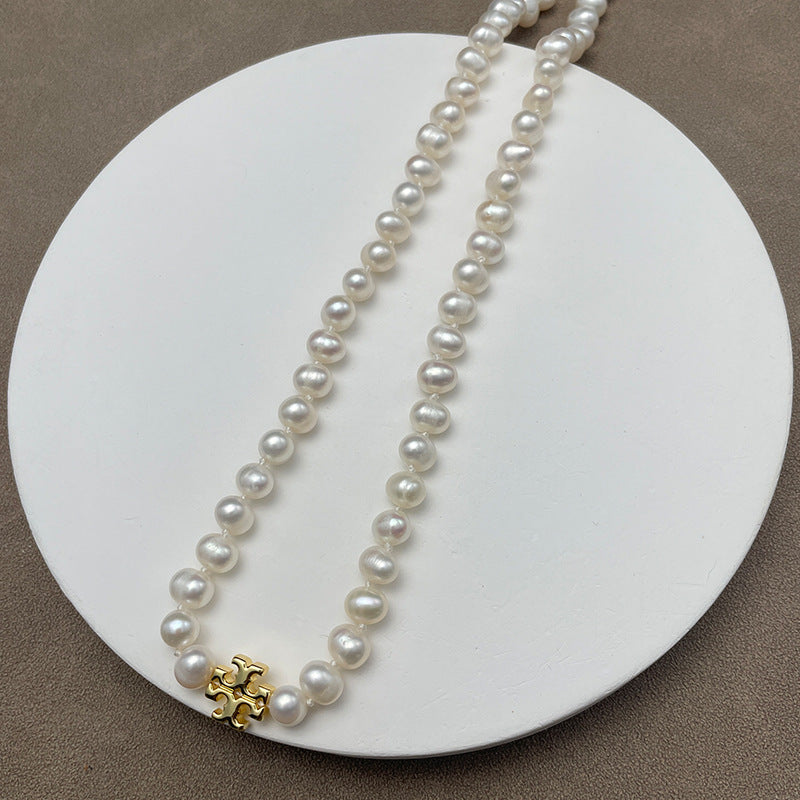 Necklace laid flat on a neutral, textured backdrop (e.g., light gray marble or linen), highlighting the contrast between the gold chevron and the pearl’s luster.