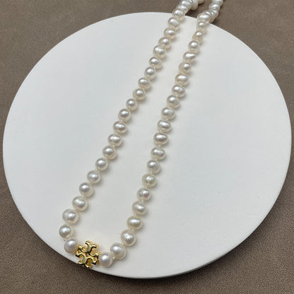 Necklace laid flat on a neutral, textured backdrop (e.g., light gray marble or linen), highlighting the contrast between the gold chevron and the pearl’s luster.
