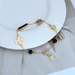 Bracelet laid in a naturally scattered, curved shape on a textured neutral background, highlighting the asymmetric placement of beads and charms.