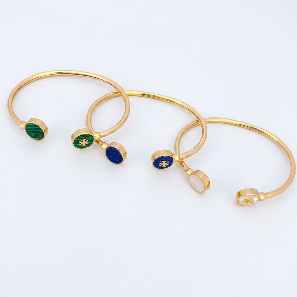 Four gold-plated open bangle bracelets with small oval enamel charms in green, blue, and white, arranged on a plain white background.