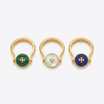 Three gold-toned ring-shaped earrings with round bezel-set stones, shown on a light gray background. The left earring has a green stone, the center has a white stone, and the right has a deep blue stone, each with a gold cross motif in the center.