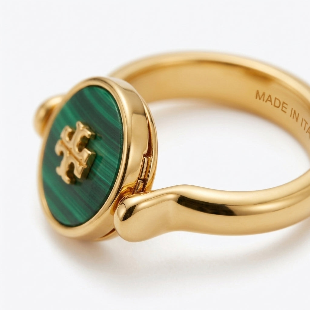 A gold ring featuring a round green malachite inlay with a gold monogram logo, shown on a clean white background.