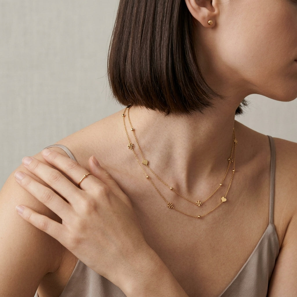 A close-up lifestyle shot of a model wearing a delicate gold double-layer necklace with small star and heart charms, along with a matching gold ring.