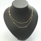 A delicate two-layered gold necklace with small heart and flower motifs, displayed on a matte black jewelry bust against a white background.