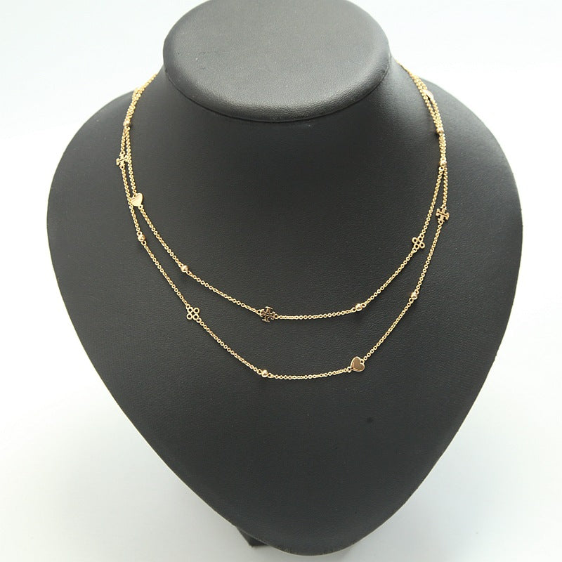 A delicate two-layered gold necklace with small heart and flower motifs, displayed on a matte black jewelry bust against a white background.