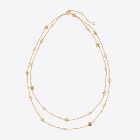 A delicate double-strand gold necklace featuring small heart and flower charms, displayed on a clean, light gray background.