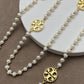 Necklace laid flat in a draped or straight line, clearly showing the repeating logo charms and the cross pendant at the center or end.