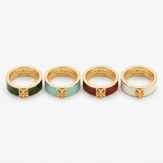 Four gold-tone Tory Burch rings with colorful enamel inlays (green, light blue, burgundy, and white) arranged in a row on a light gray background.