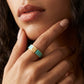 A close-up of a model's hand wearing a gold ring with a turquoise blue inlay, resting near her chin.
