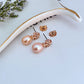 Clean, vertical shot of a single earring against a soft, neutral background, clearly showing the Double T logo above the pearl drop.