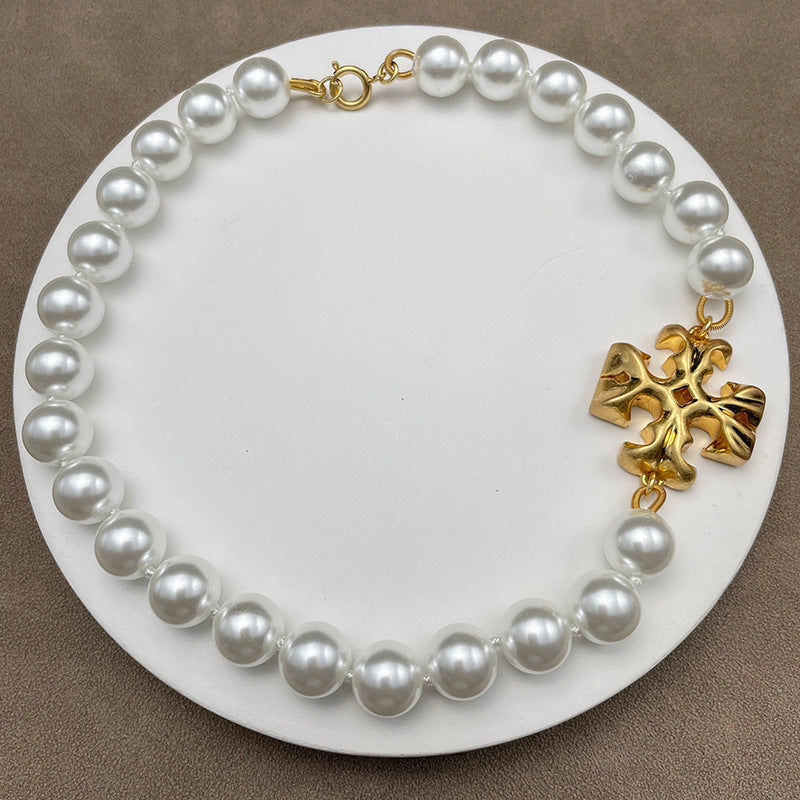 Necklace laid flat on a soft, neutral background (light gray or ivory), clearly showing the Double T logo and pearl together on the chain.