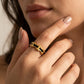 A close-up of a model's hand wearing a gold ring with black rectangular inlays, set against her face and neck.