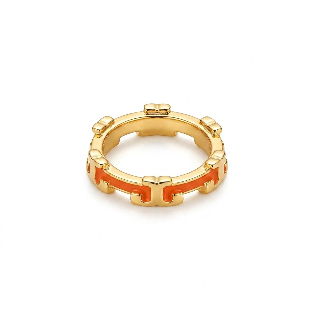 A gold-plated ring with a repeating geometric pattern and bright orange inlay accents, shown on a plain white background.