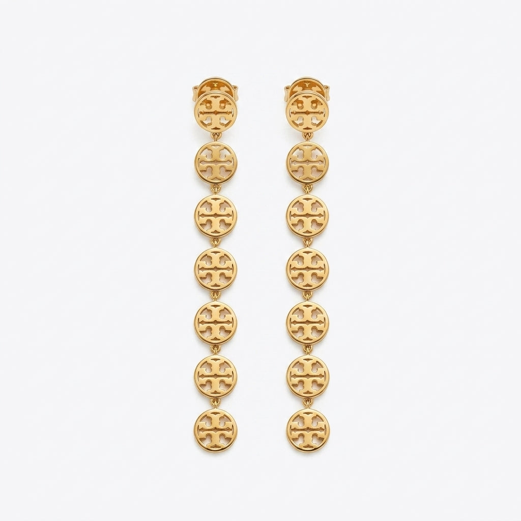 A pair of gold dangle earrings featuring a vertical chain of oval links, each engraved with the signature interlocking Tory Burch logo, set against a plain light gray background.