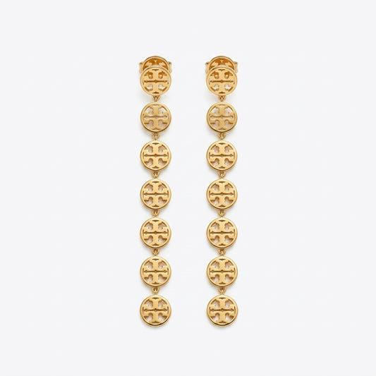 A pair of gold dangle earrings featuring a vertical chain of oval links, each engraved with the signature interlocking Tory Burch logo, set against a plain light gray background.