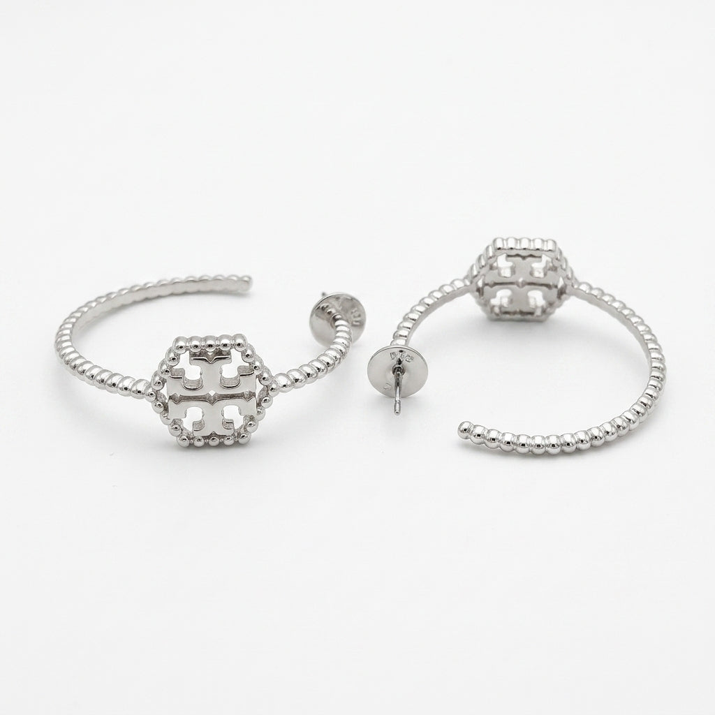A pair of silver-toned hoop earrings with a textured beaded band and a central geometric openwork charm, shown on a plain white background.